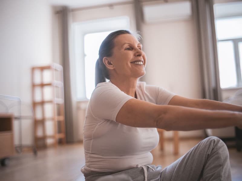 A woman seated at home, reaching forward with both arms.